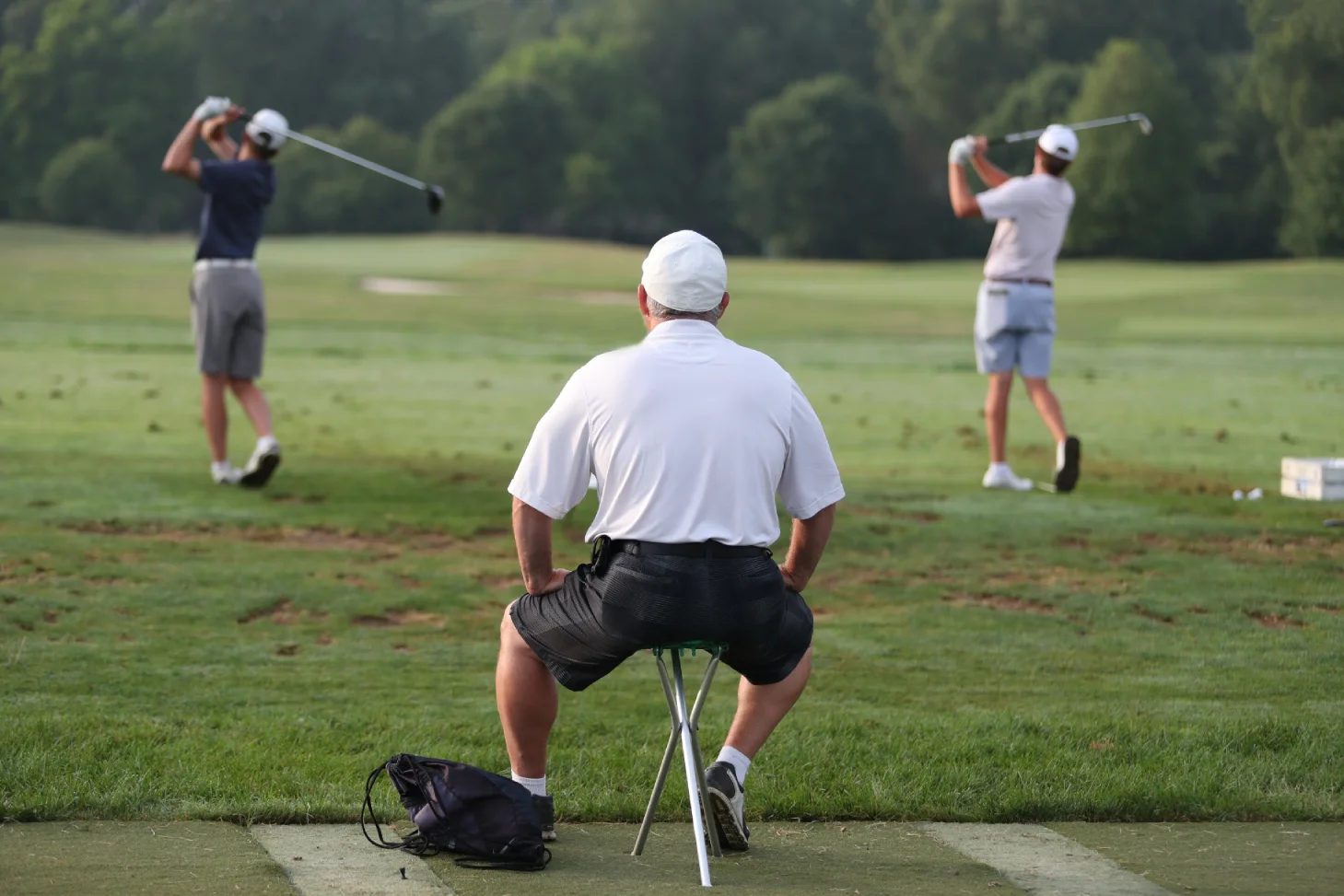 Golf instructor watching two players practice their swing at a driving range during a spring golf resort vacation